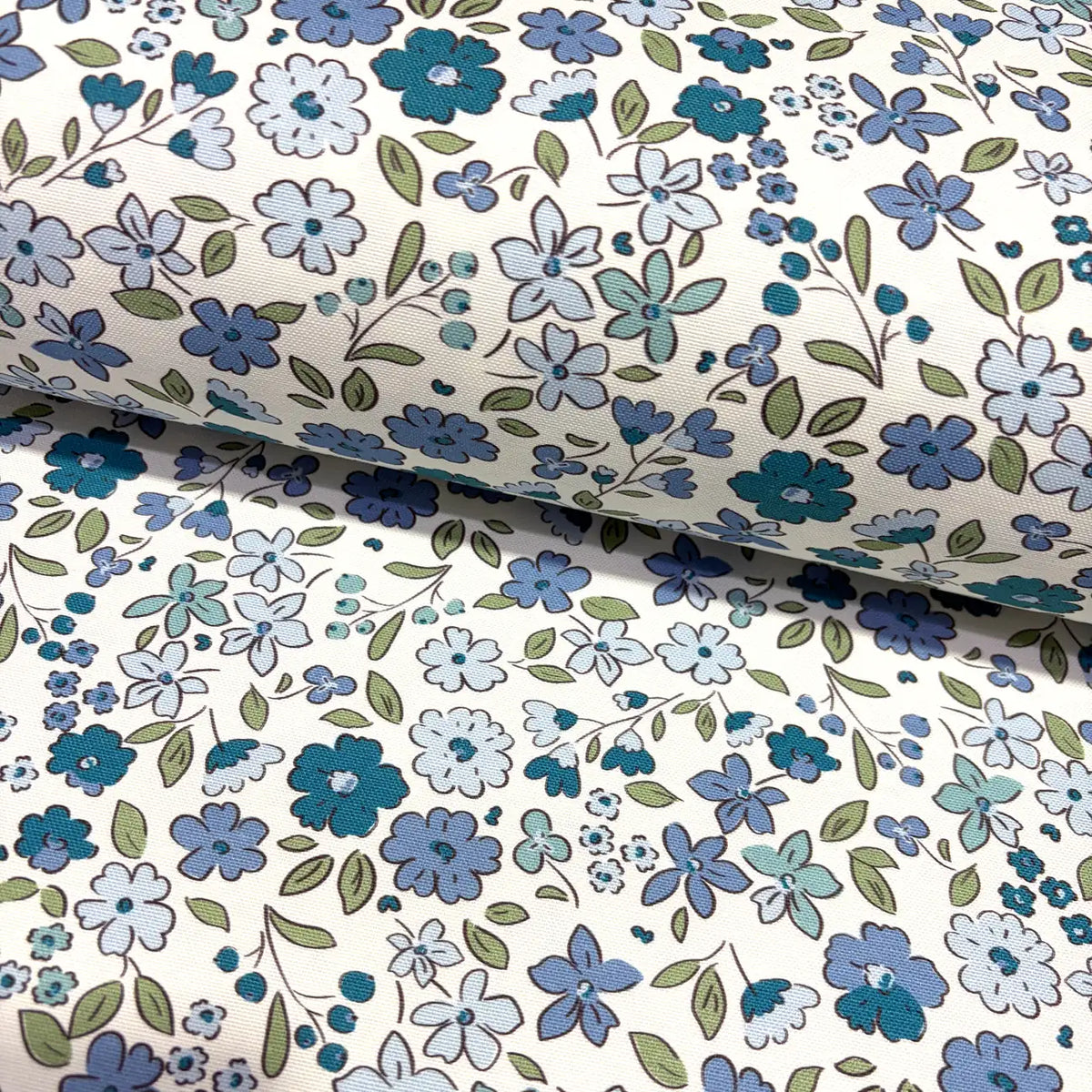 Floral fabric patterned with denim blue flowers and green leaves on a white background.