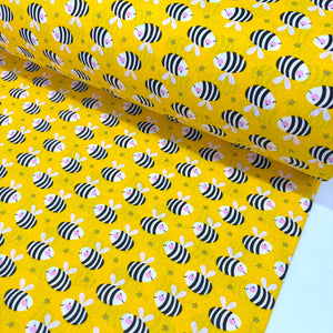 Bumble bee cotton fabric featuring black and white striped bees on a bright yellow background, ideal for quilting, children's sewing, nursery décor and craft projects.
