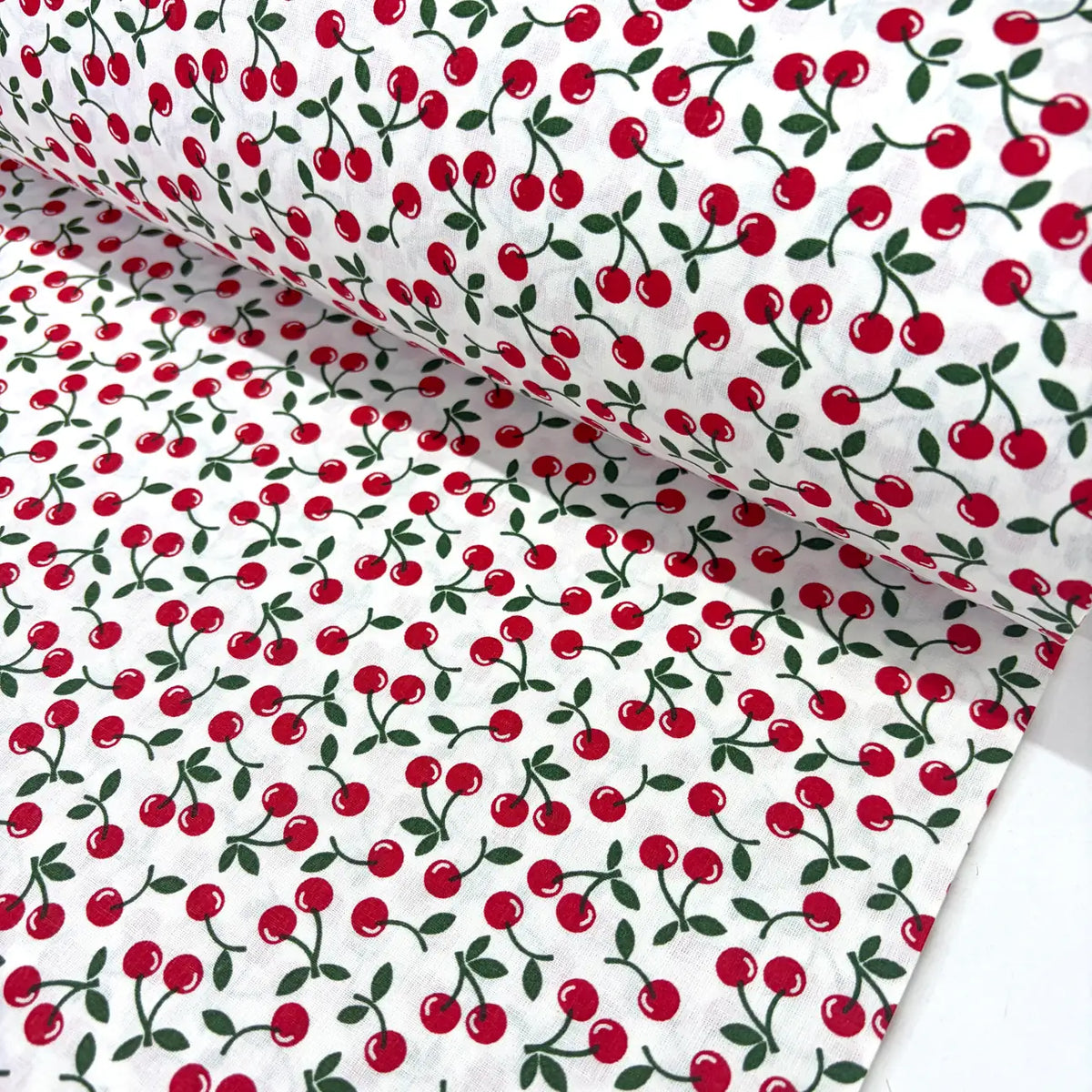 Retro vintage cotton poplin fabric featuring an all-over red cherry fruit print with green leaves on a white background. 