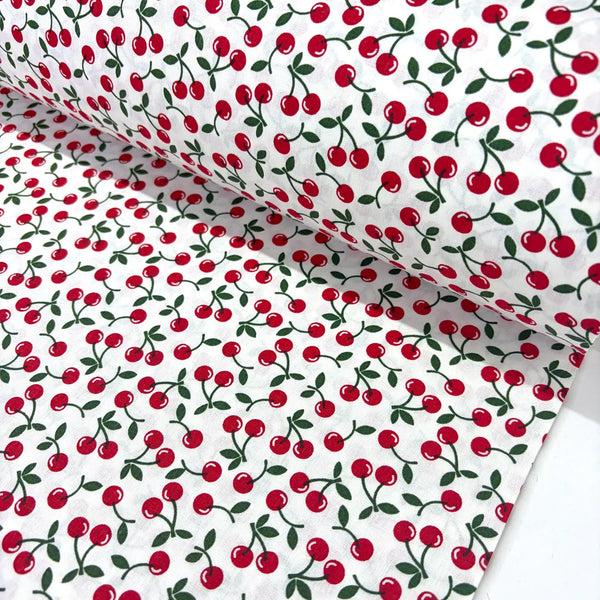 Retro vintage cotton poplin fabric featuring an all-over red cherry fruit print with green leaves on a white background. 