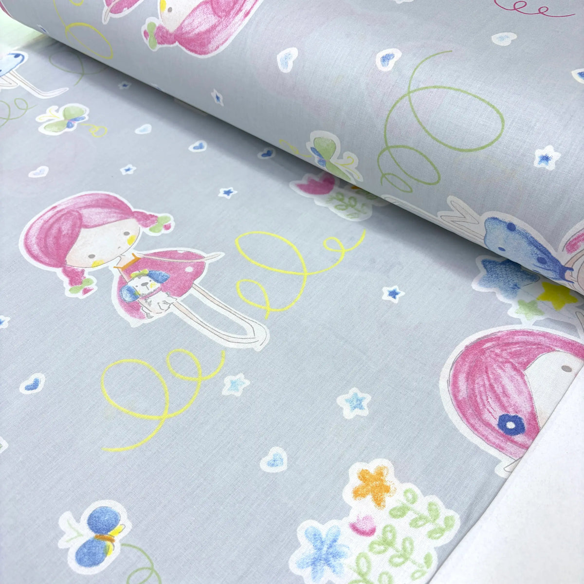 Children's cotton poplin fabric with cartoon characters and colorful patterns on a light blue background.