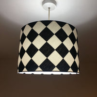 Geometric checkered lampshade with black and white pattern on a plain background with lights on.