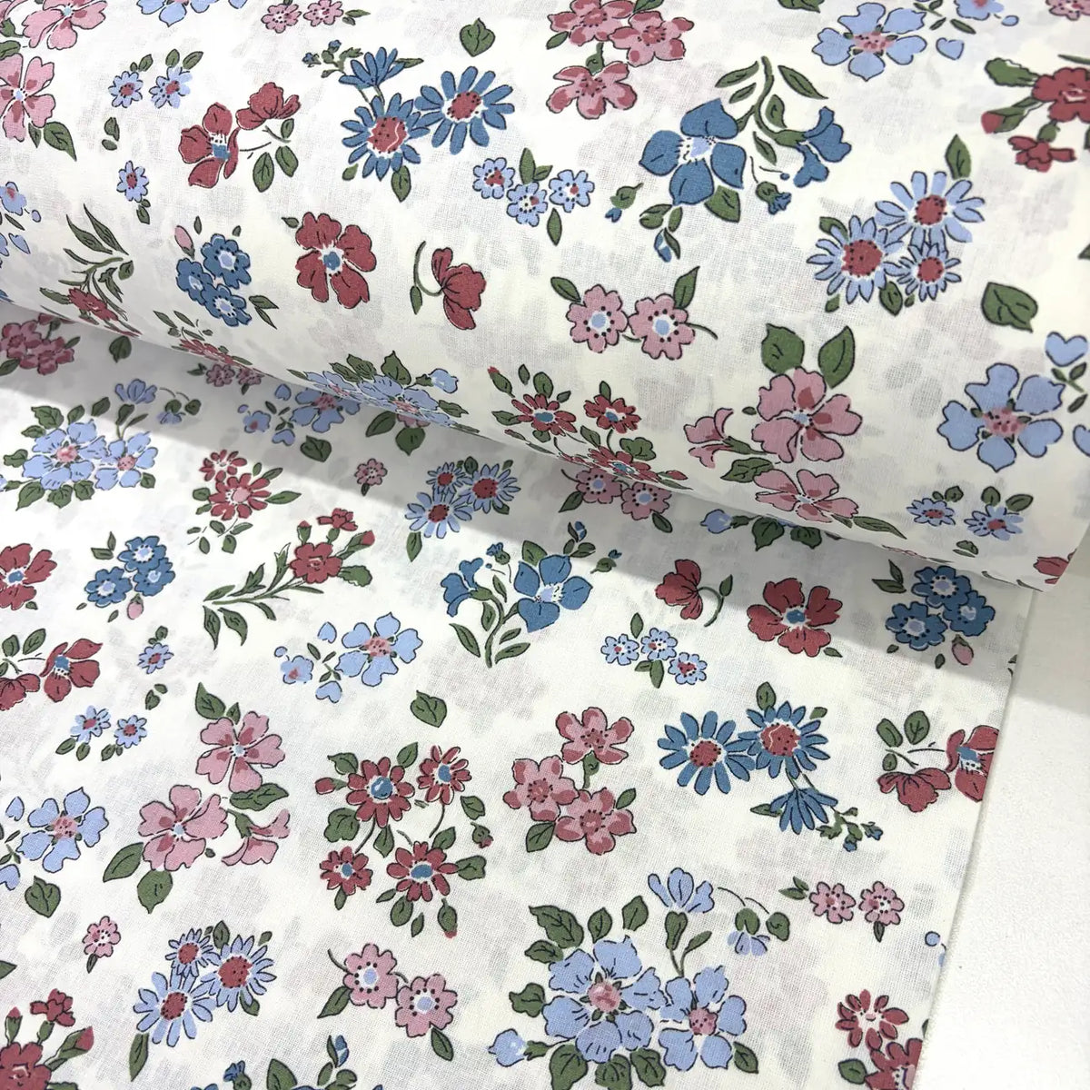 Ditsy floral cotton fabric patterned with blush pink, burgundy and blue flowers on a white background.