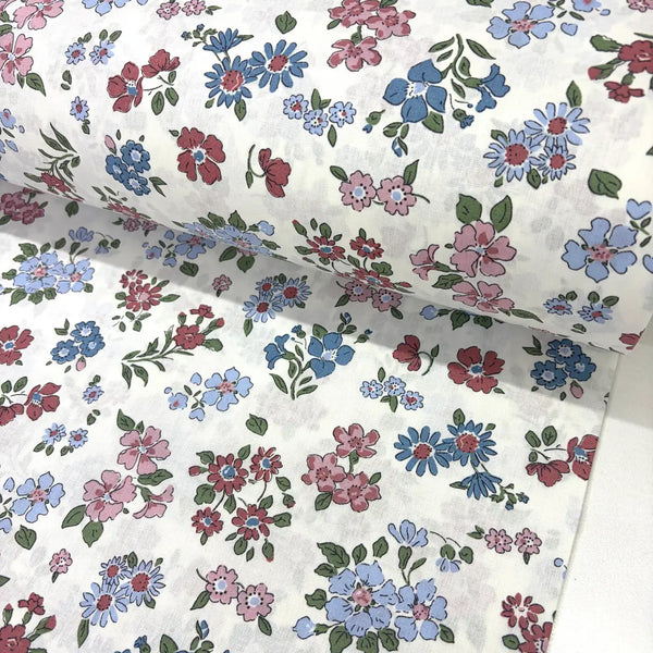 Ditsy floral cotton fabric patterned with blush pink, burgundy and blue flowers on a white background.