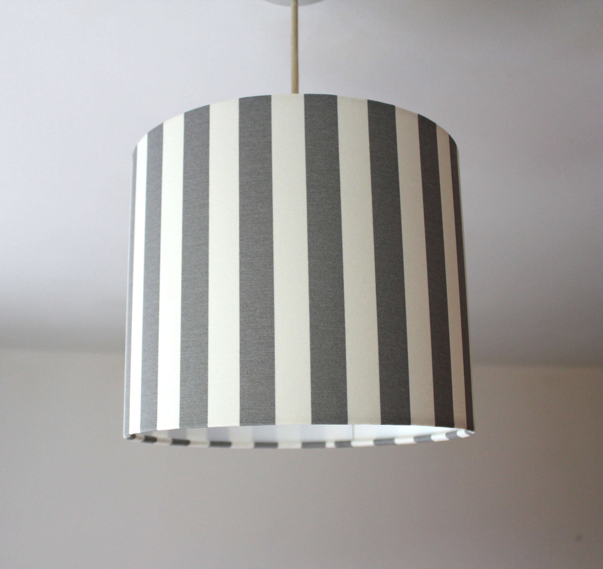 Striped ceiling lampshade with grey and white vertical stripes on a plain background.