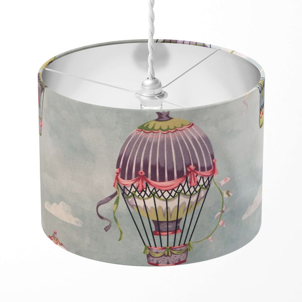 A drum lampshade with a baby blue colour featuring a hot air balloon design with a patterned border.