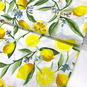 Lemon blossom cotton fabric featuring yellow lemons, citrus slices, blue flowers and green leaves on a white background.