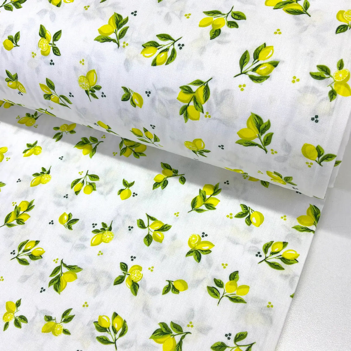 Mini lemon print cotton fabric featuring small yellow lemons and green leafy sprigs on a white background.