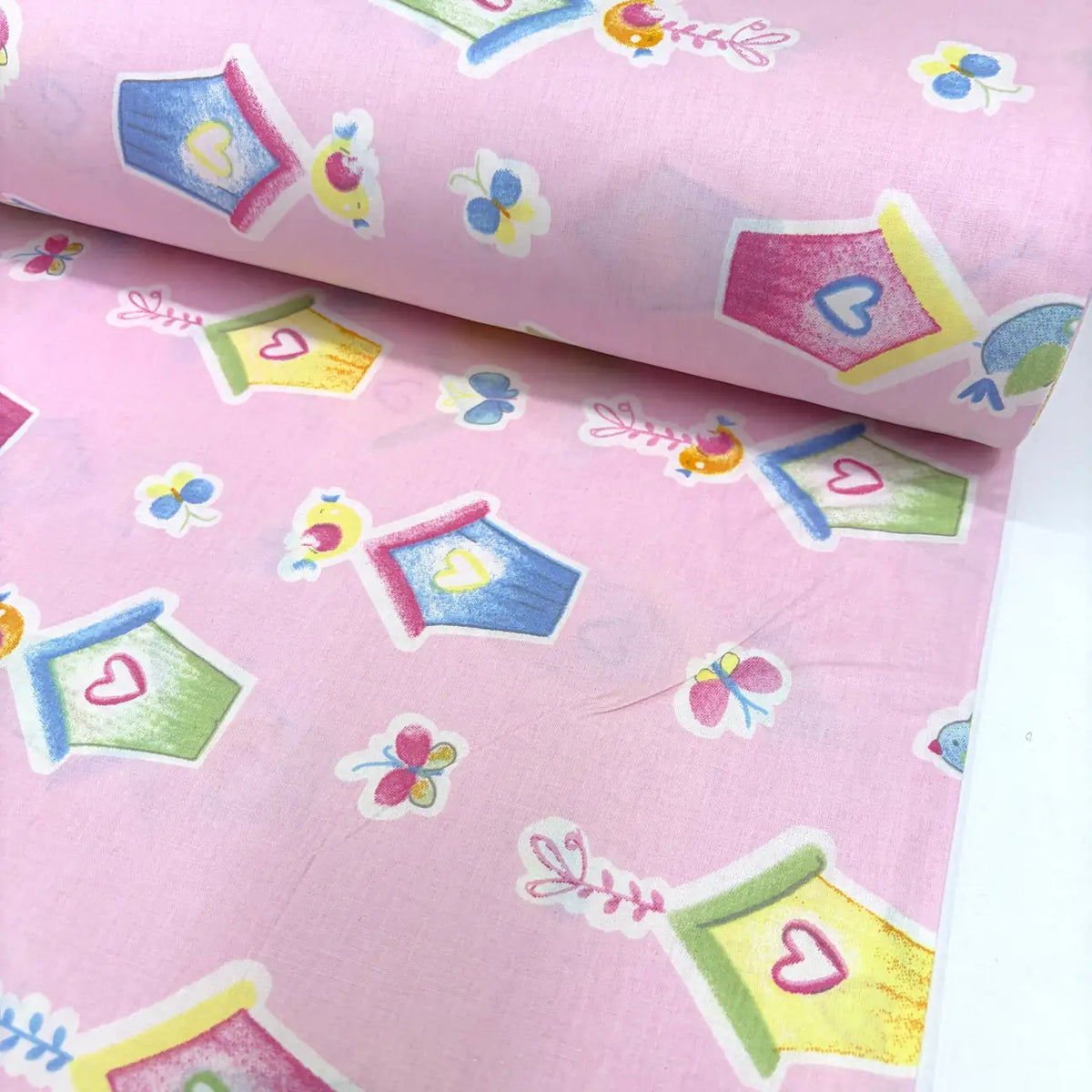 Pink cotton poplin fabric with colorful birdhouse, butterfly and heart patterns.