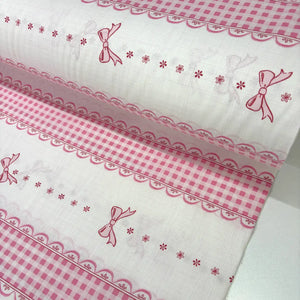 Pink bow and gingham check 100% cotton poplin fabric with lace-effect border stripes on a white background, ideal for girls' dressmaking, quilting, bedding, and nursery sewing projects.