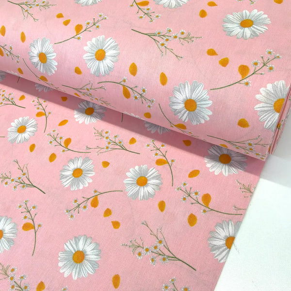 Pink daisy cotton fabric featuring large white daisies with yellow centres, delicate wildflowers and scattered petals on a soft pink background, ideal for dressmaking, quilting and craft projects.