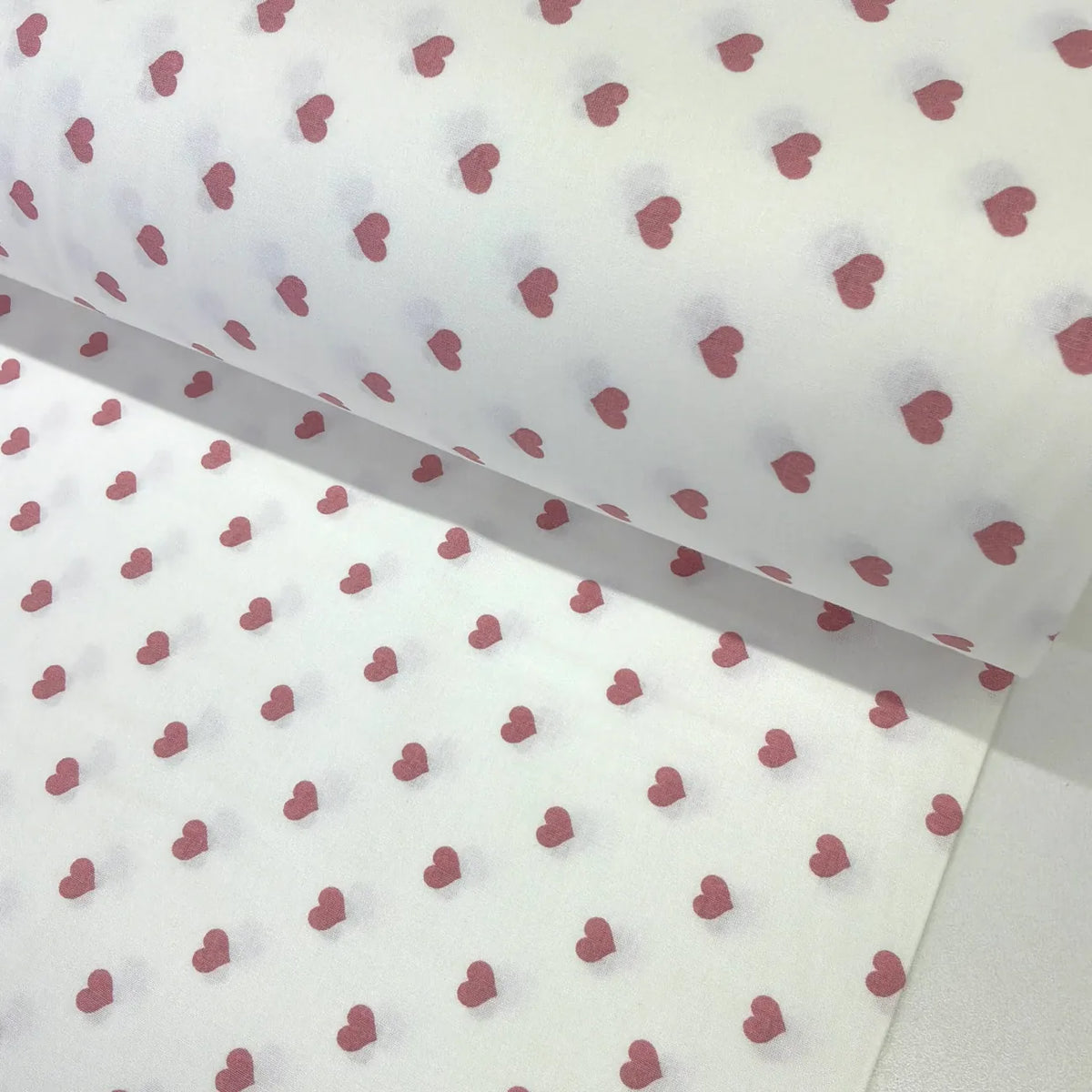 Cotton poplin fabric patterned with dusty pink heart prints on a white background.