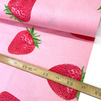 Pink fabric with a repeating red strawberry print, shown with a wooden ruler to indicate scale.