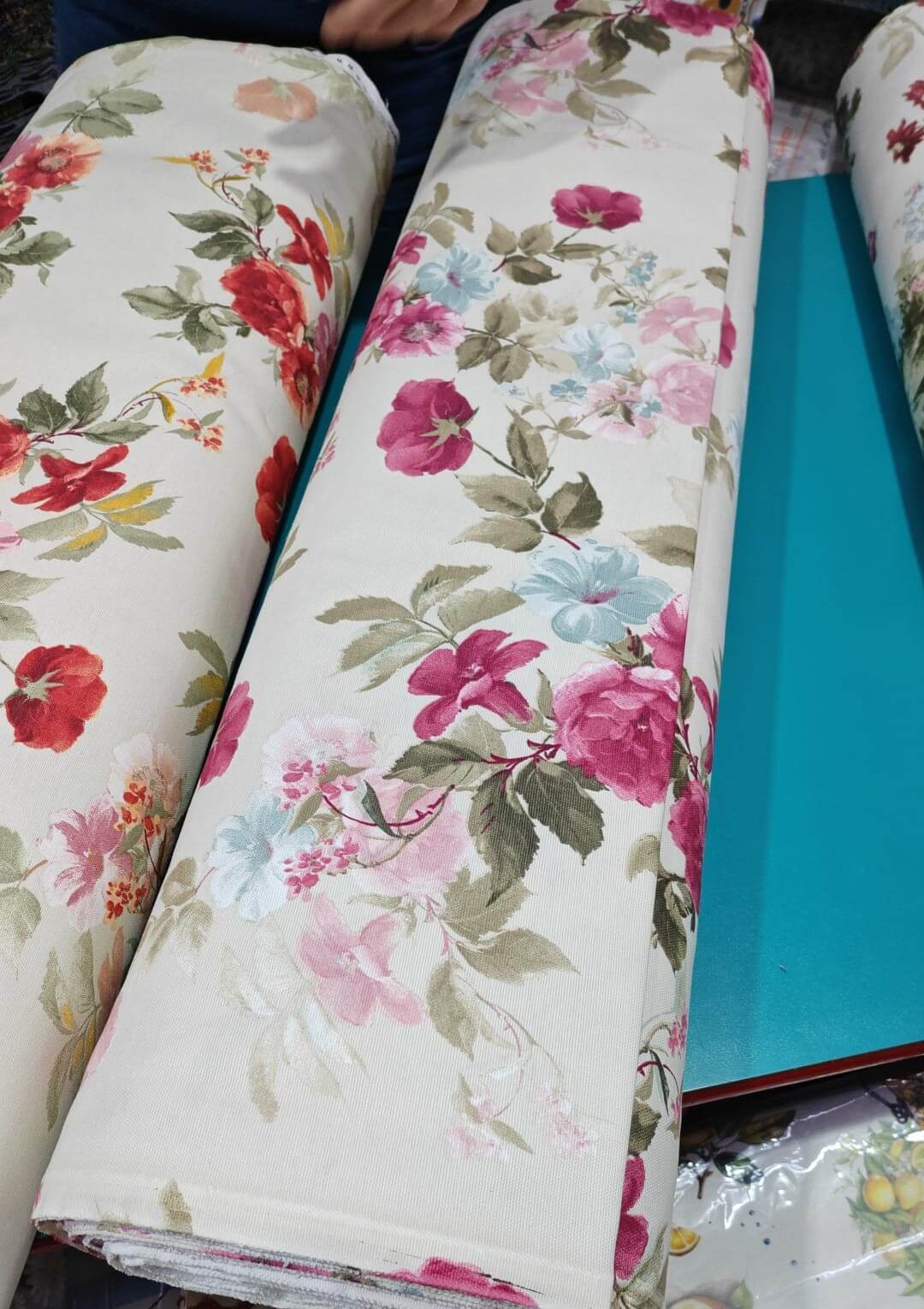 Rolls of floral-patterned upholstery fabric with a blue desk underneath.