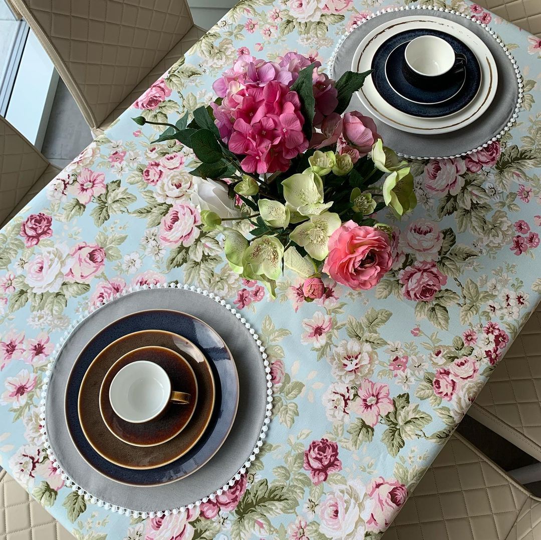Table setting with pink floral tablecloth, plates, and flowers.