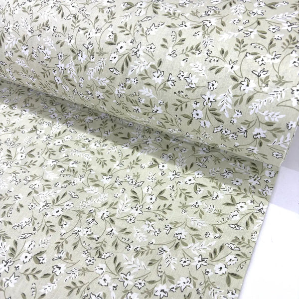 Floral patterned fabric with small white flowers and green leaves on a light sage green background.
