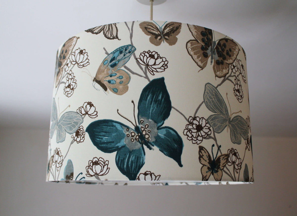Denim blue and beige ceiling lampshade with butterfly and floral pattern on a plain background.