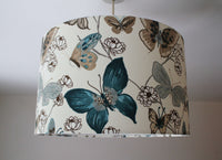 Denim blue and beige ceiling lampshade with butterfly and floral pattern on a plain background.