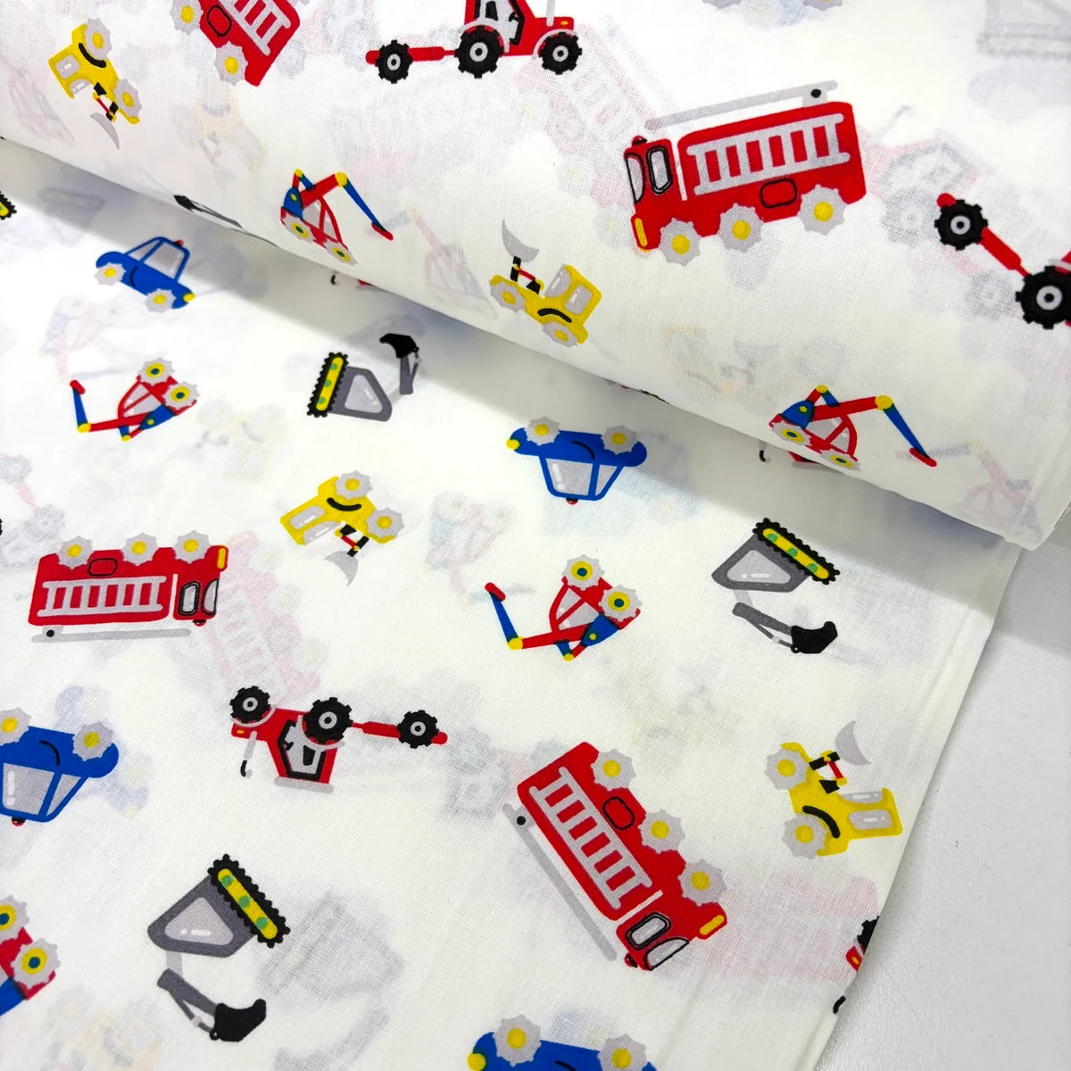 Construction vehicles cotton fabric featuring colourful fire engines, diggers, tractors, cars and tools on a white background.