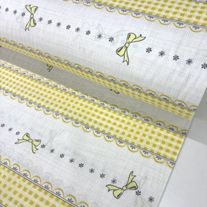 Yellow gingham check cotton poplin fabric with ribbon bows and lace-effect border stripes on a white background.