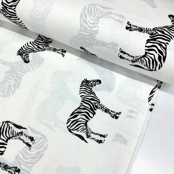 Black and white zebra print cotton fabric featuring safari zebras on a white background.