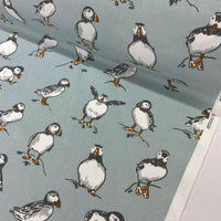 A close-up of fabric featuring a repeating print of puffins on a muted blue-gray background. 
