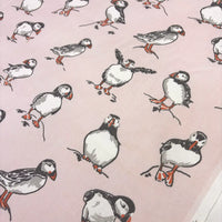 A close-up of a light pink fabric printed with illustrated puffins in black, white, gray, and orange.