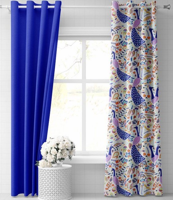 A brightly lit room setting showcasing a mix of solid and patterned curtain fabric panel options. On the left, a vibrant royal blue eyelet curtain fabric panel hangs elegantly from a silver rod. On the right, a coordinating panel is made from a decorative printed upholstery fabric featuring a colorful peacock and floral botanical motif on a cream background.