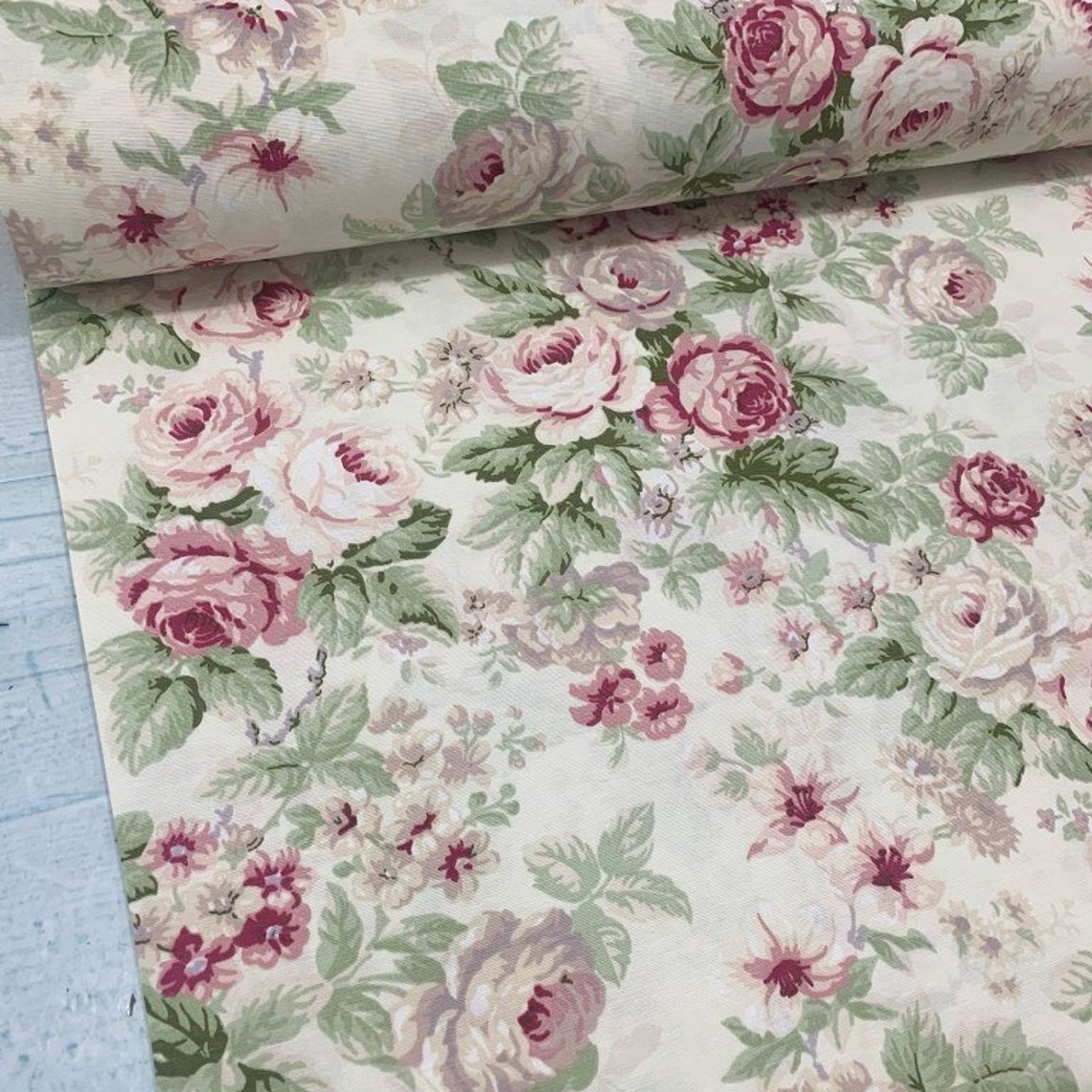 Cream upholstery fabric patterned with pink roses and green leaves.